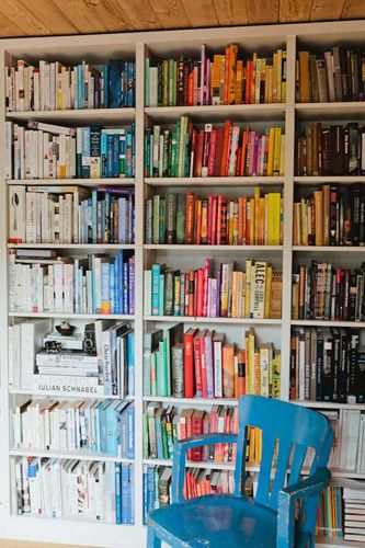 a book shelf filled with lots of books next to a blue chair in front of it