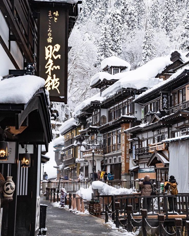 people are standing outside in the snow next to some wooden buildings with chinese writing on them