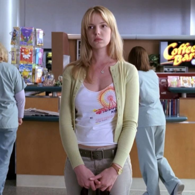 a woman standing in front of a counter at a store with people walking around her