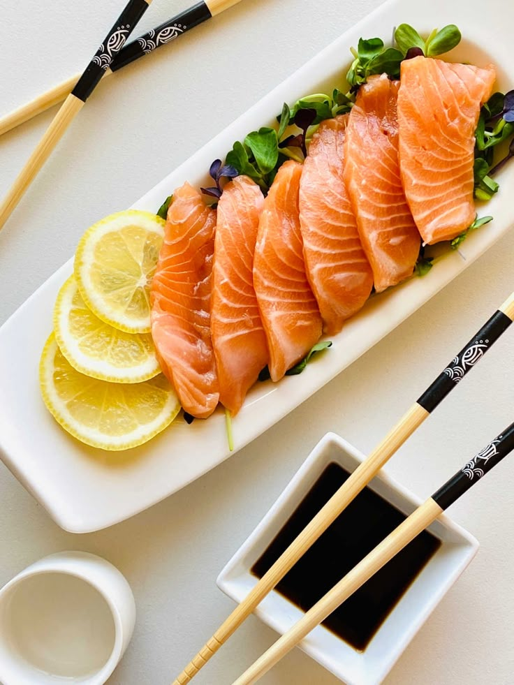 salmon sashimi on a plate with lemons and chopsticks next to it