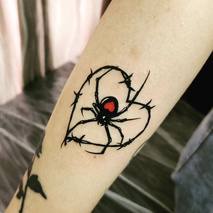 a spider tattoo on the arm with barbed wire and red heart in it's center