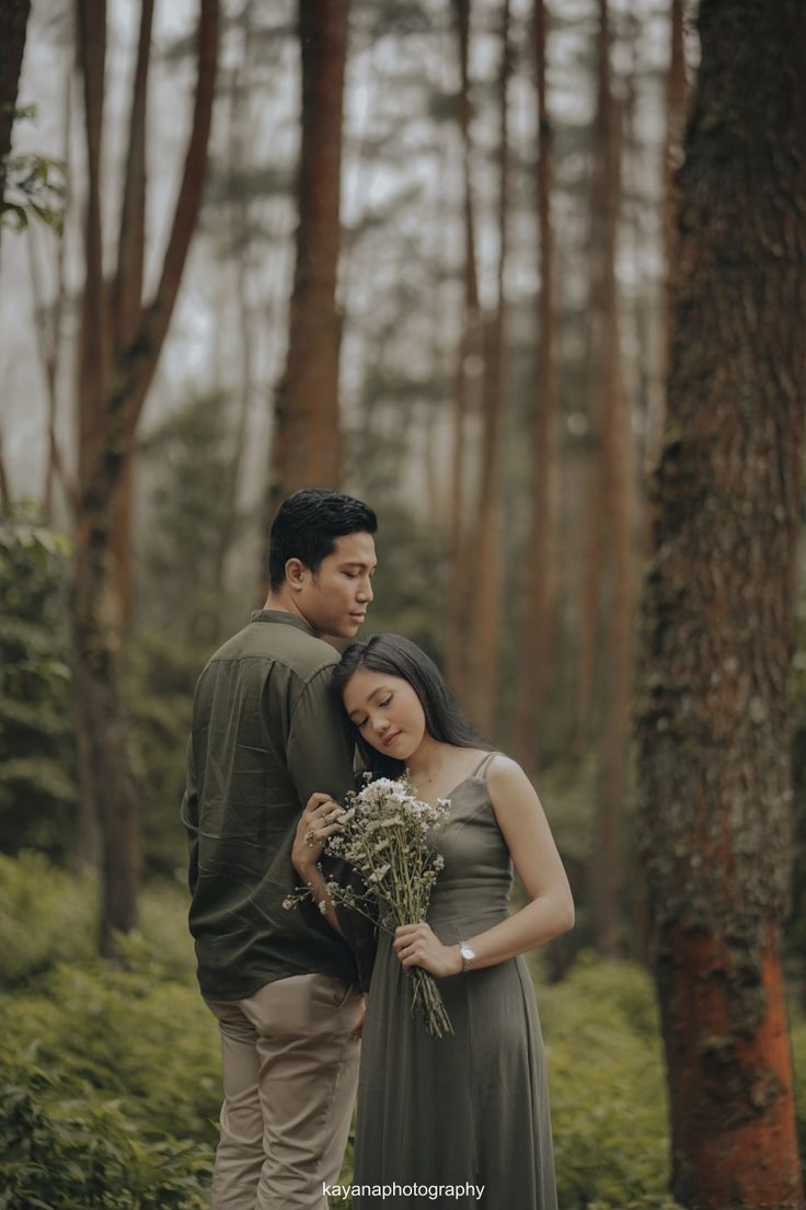 a man and woman standing next to each other in the woods