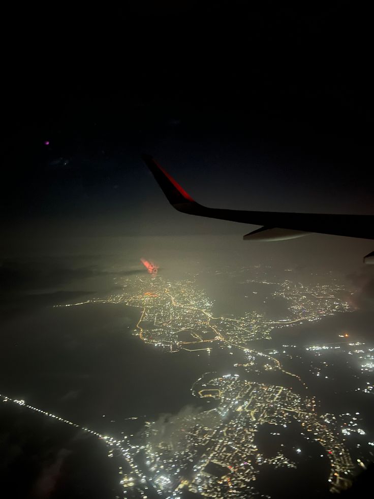 an airplane wing flying over a city at night with lights on the ground and in the air