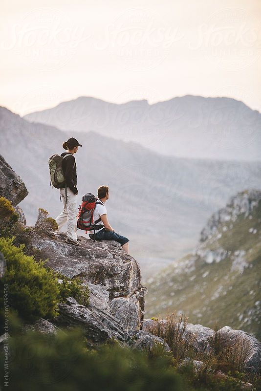 two people sitting on top of a mountain looking at the valley below by jovan for stocks