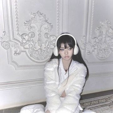 a woman sitting on the floor with headphones in her ears wearing a white coat