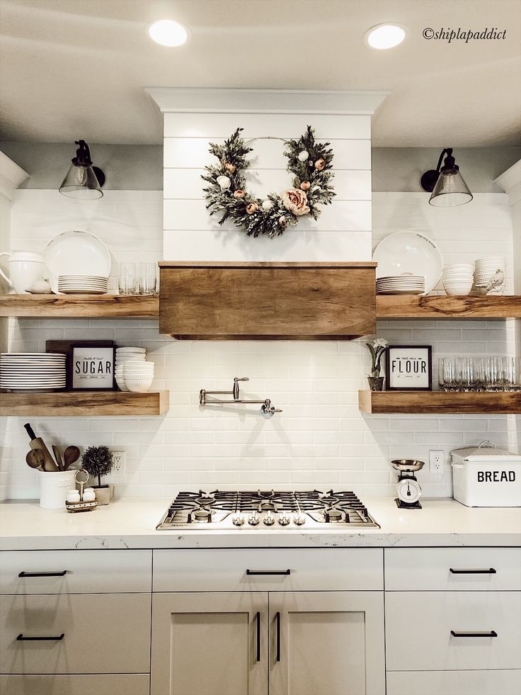 a white kitchen with open shelving above the stove and shelves on the wall, decorated with wreaths