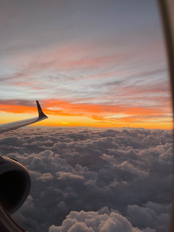 an airplane wing flying above the clouds at sunset