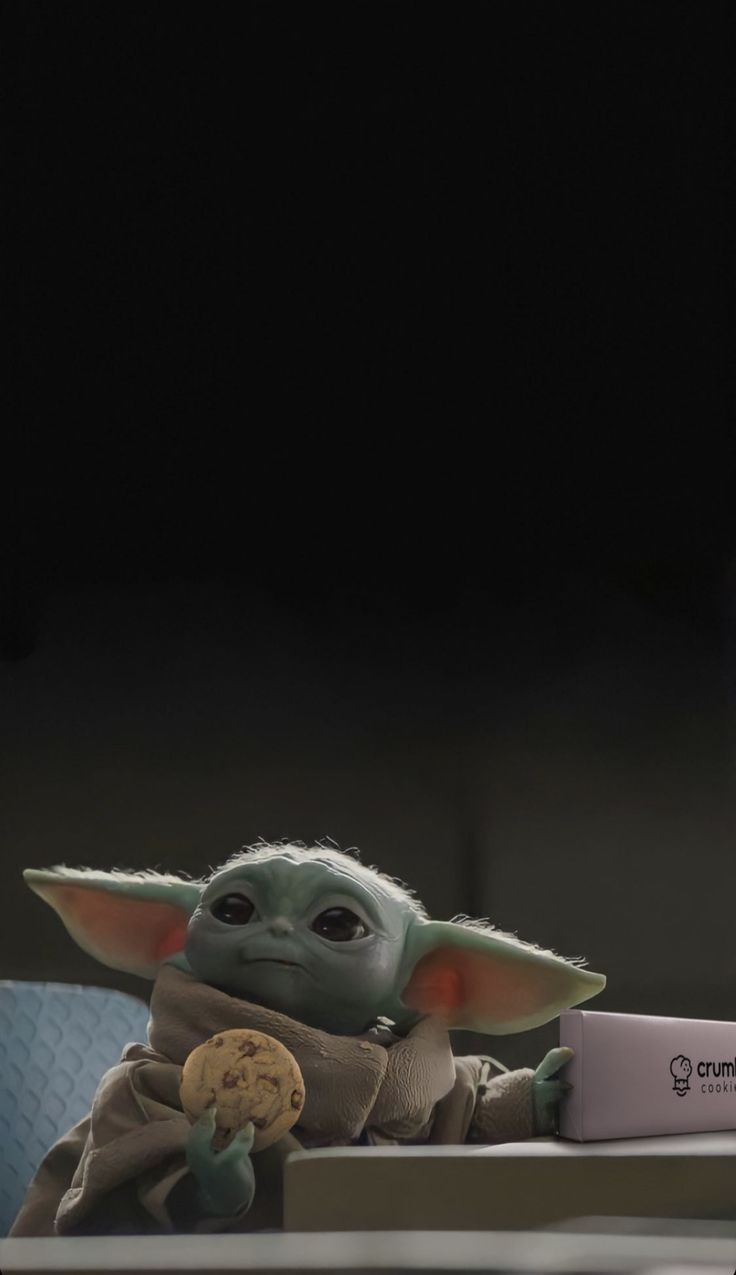 the child yoda is holding a cookie and looking at something in front of him