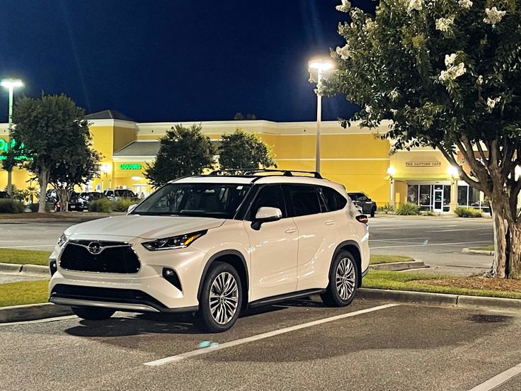 a white suv is parked in a parking lot at night time with the lights on