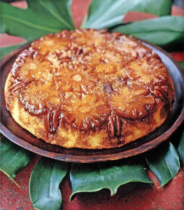 a cake sitting on top of a wooden plate next to green leafy plants and leaves