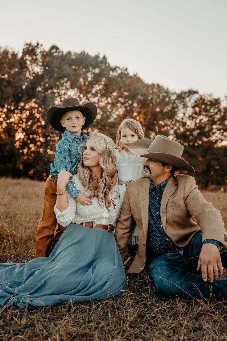 a man, woman and two children sitting on the ground in a field at sunset