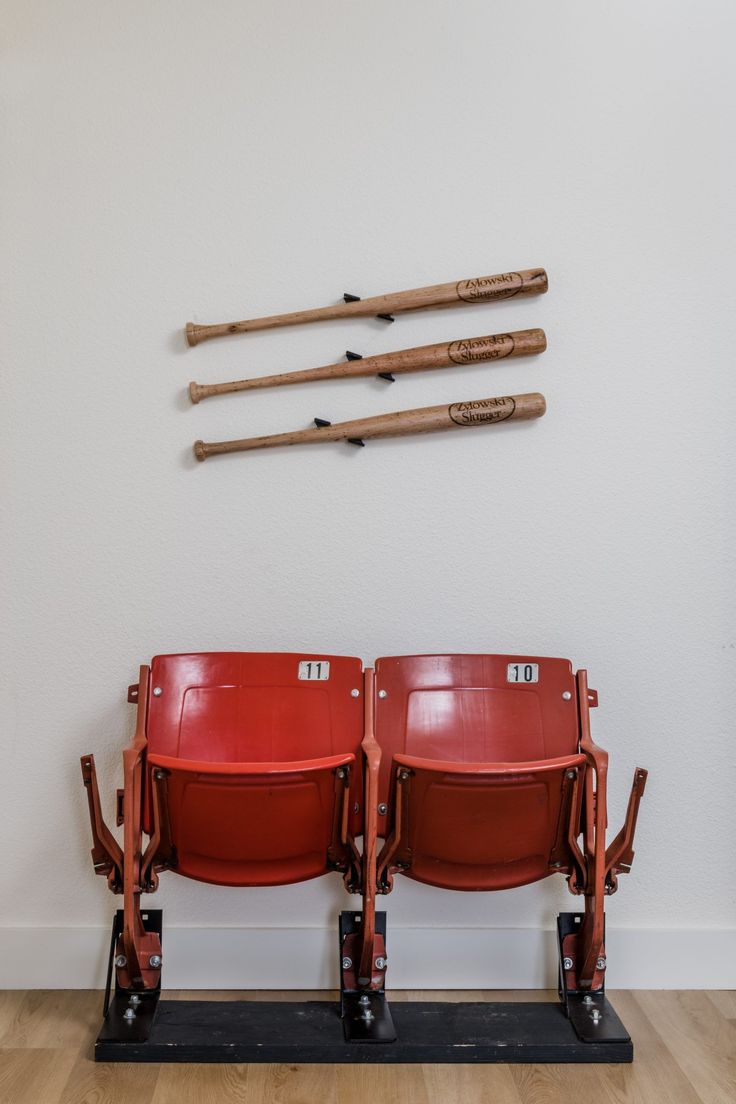 three red seats with baseball bats mounted to the wall behind them in front of a white wall