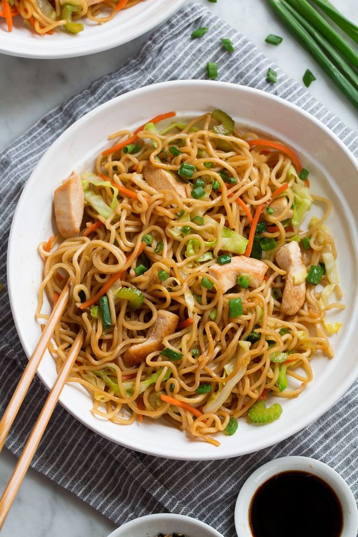 two bowls filled with noodles and vegetables on top of a table next to chopsticks