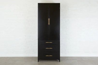 a tall black cabinet with gold handles against a white brick wall in an empty room