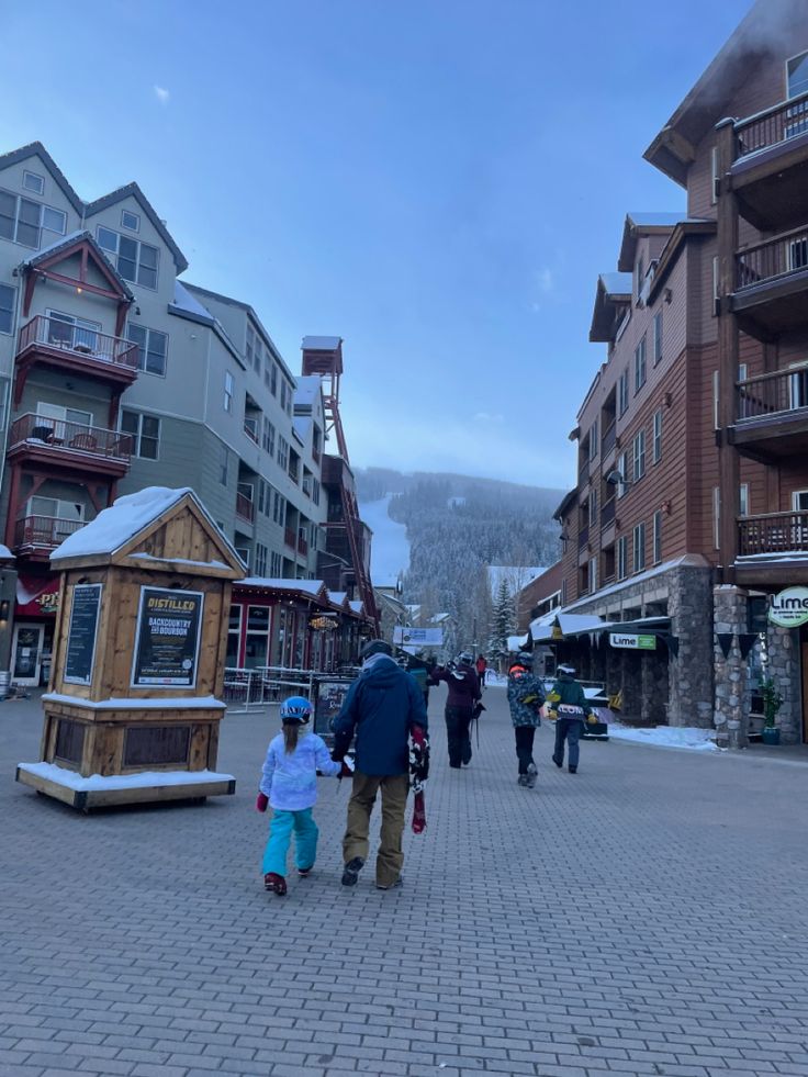 people are walking down the street in front of buildings with snow covered mountains behind them