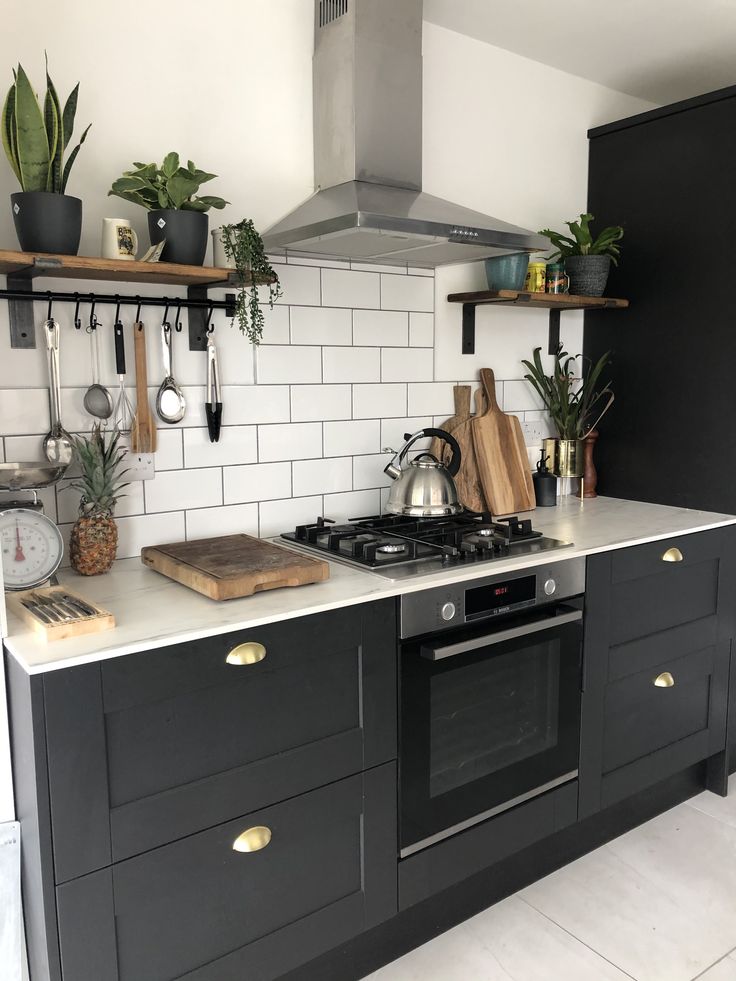 a kitchen with black cabinets and white tile backsplash, potted plants on the stove