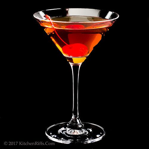 a glass filled with a drink on top of a black table next to an orange slice