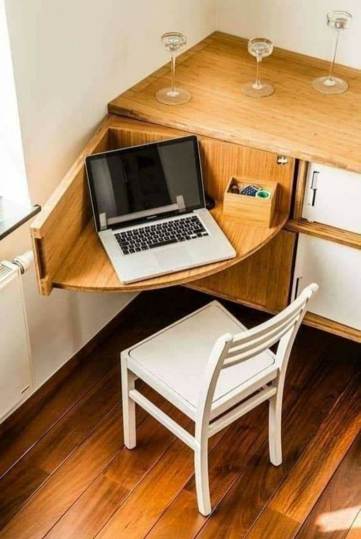 a laptop computer sitting on top of a wooden desk next to a white chair and wine glasses