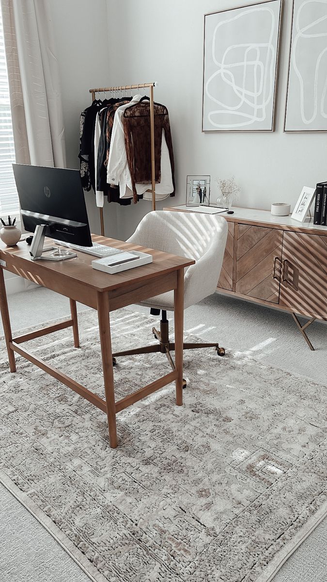 a desk with a laptop on top of it in front of a dresser and clothes rack