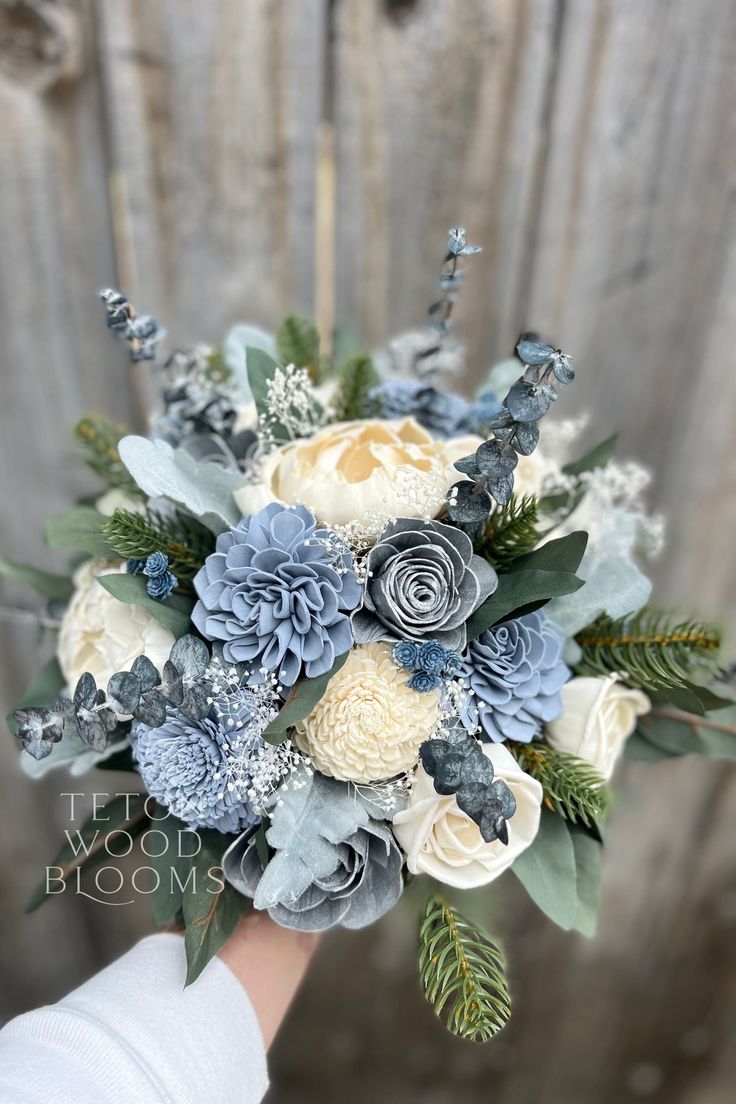 a bridal bouquet with blue flowers and greenery on the side of a wooden fence