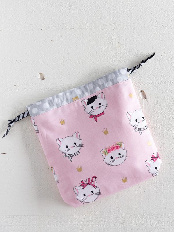 a small pink bag with cats on it hanging from a wall next to a string