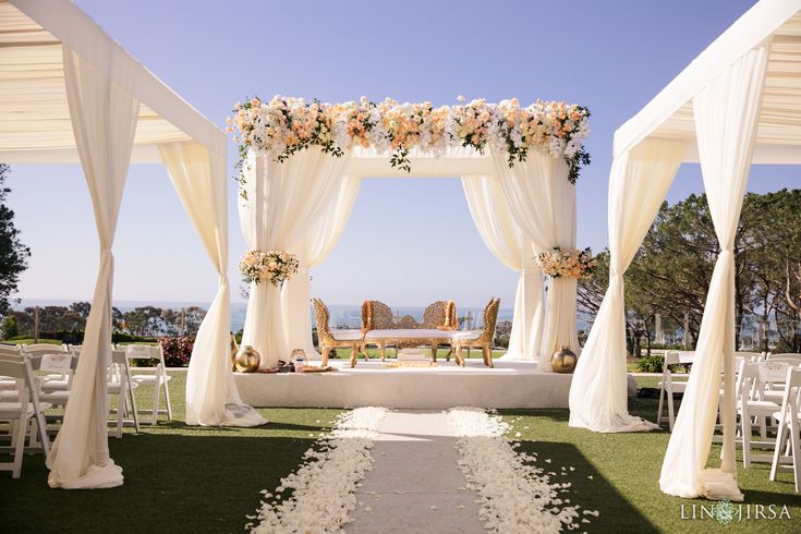 an outdoor wedding setup with white draping and flowers on the aisle, overlooking the ocean