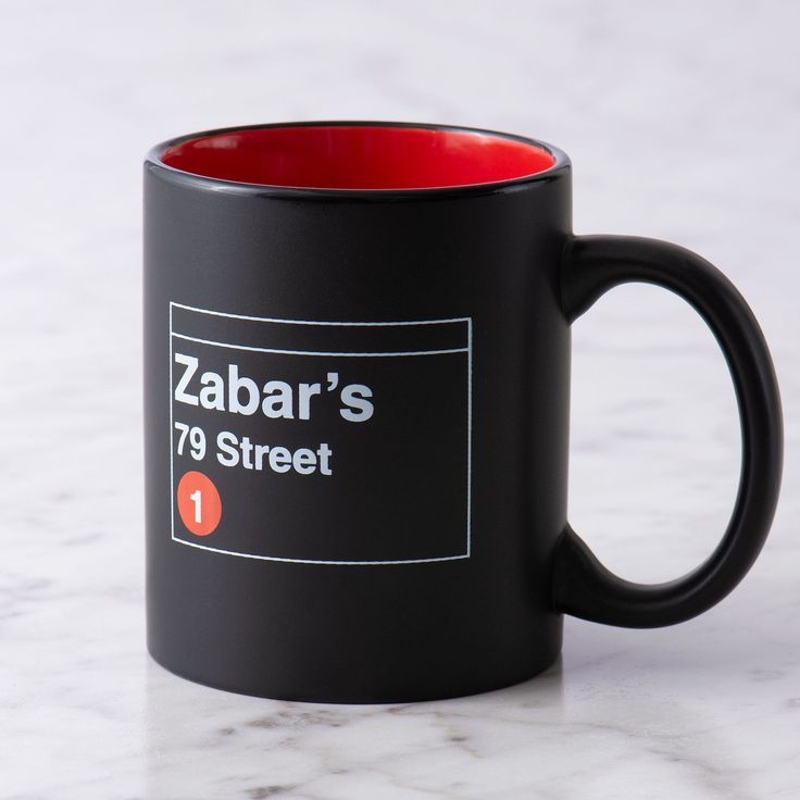 a black and red coffee mug sitting on top of a white marble counter with the name zabar's 99 street