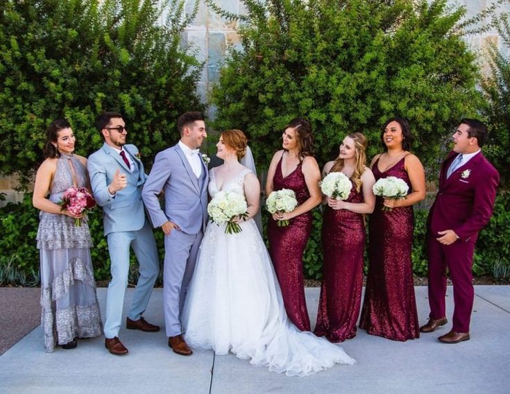 a group of people standing next to each other in front of some bushes and trees