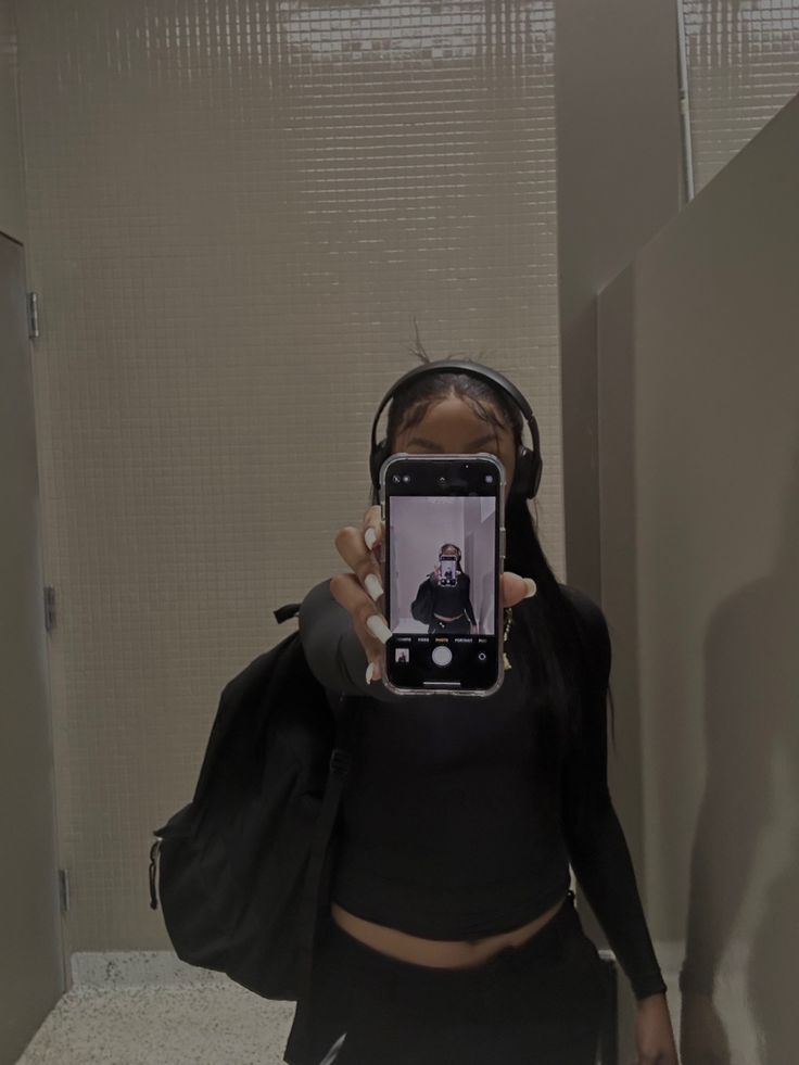 a woman taking a selfie in the bathroom with her cell phone and headphones