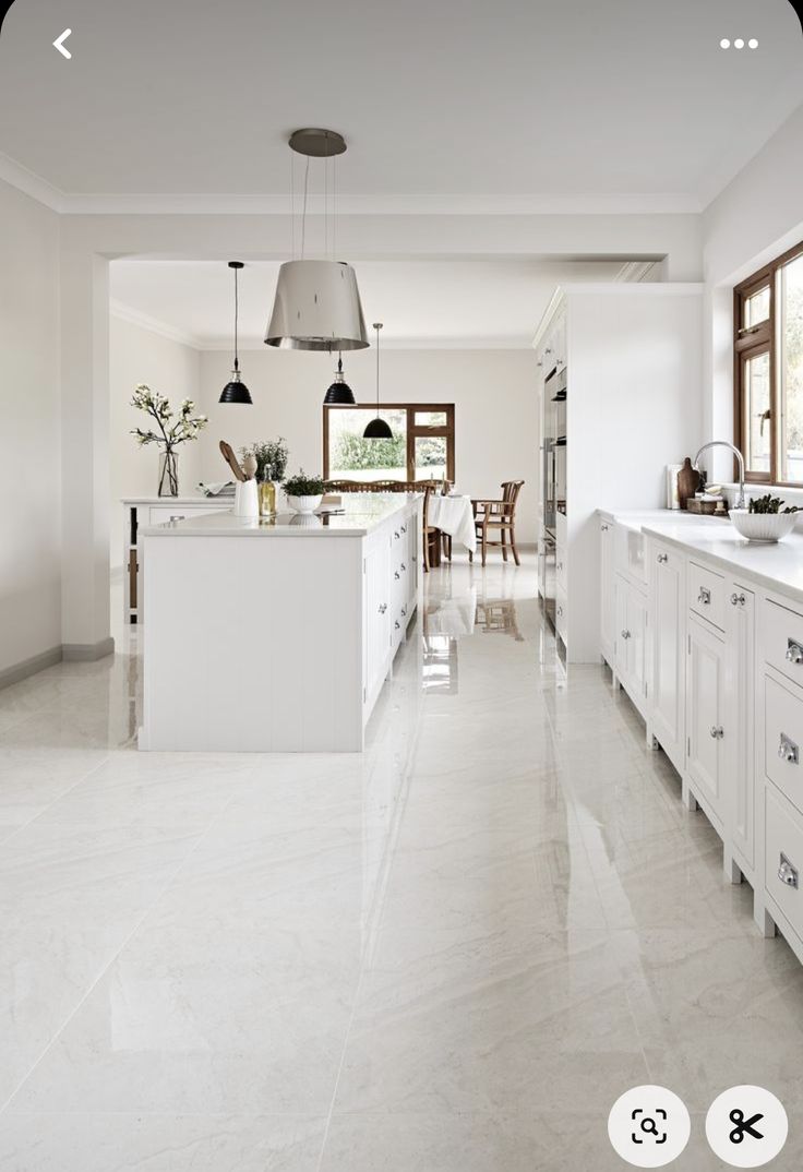 a large kitchen with white cabinets and marble flooring is shown in this image, there are two pendant lights hanging from the ceiling