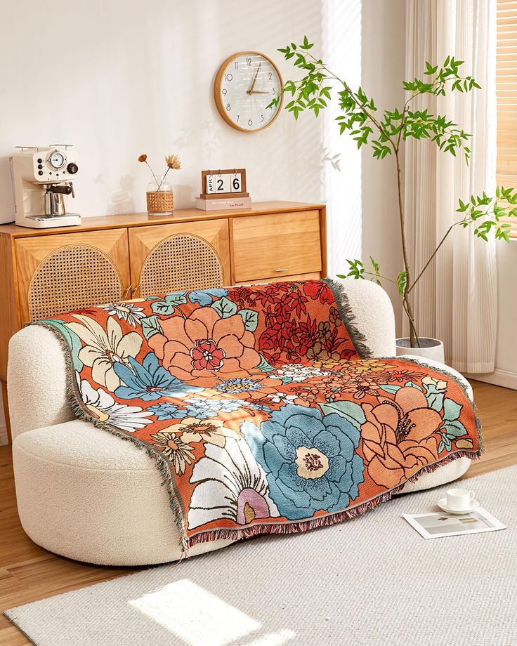 a living room with a couch covered in an orange flowered blanket next to a clock