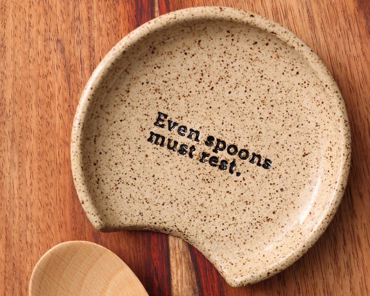 a wooden spoon sitting on top of a table next to a ceramic bowl with the words even spoone must eat