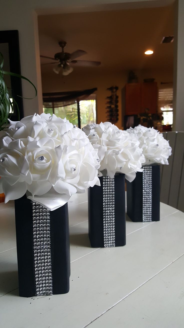 three black vases with white flowers are sitting on a table in front of a mirror