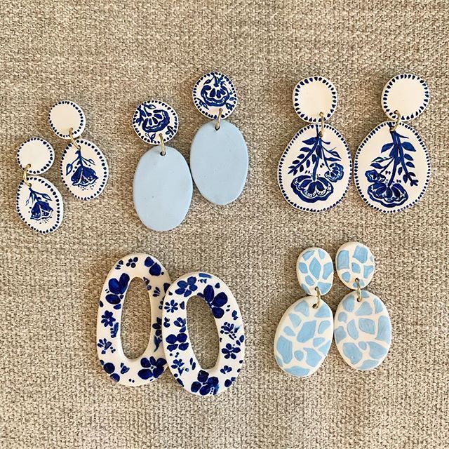 six pairs of blue and white earrings on a beige surface, including one with an oval shaped earring