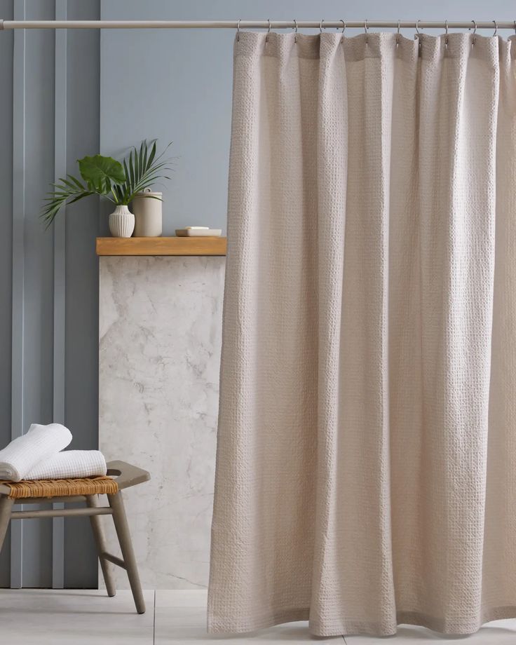 a white shower curtain in a bathroom next to a wooden stool and potted plant