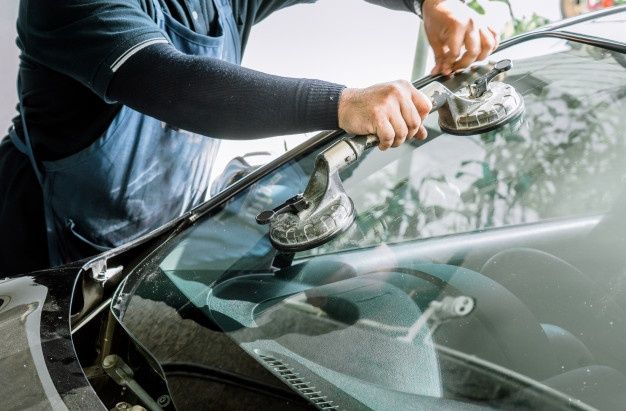 a man waxing the windshield of a car with an electric hand held polisher