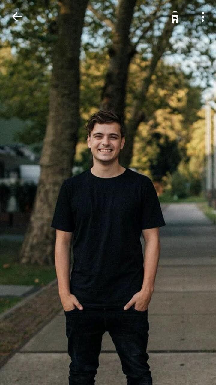 a young man standing on the sidewalk with his hands in his pockets and smiling at the camera