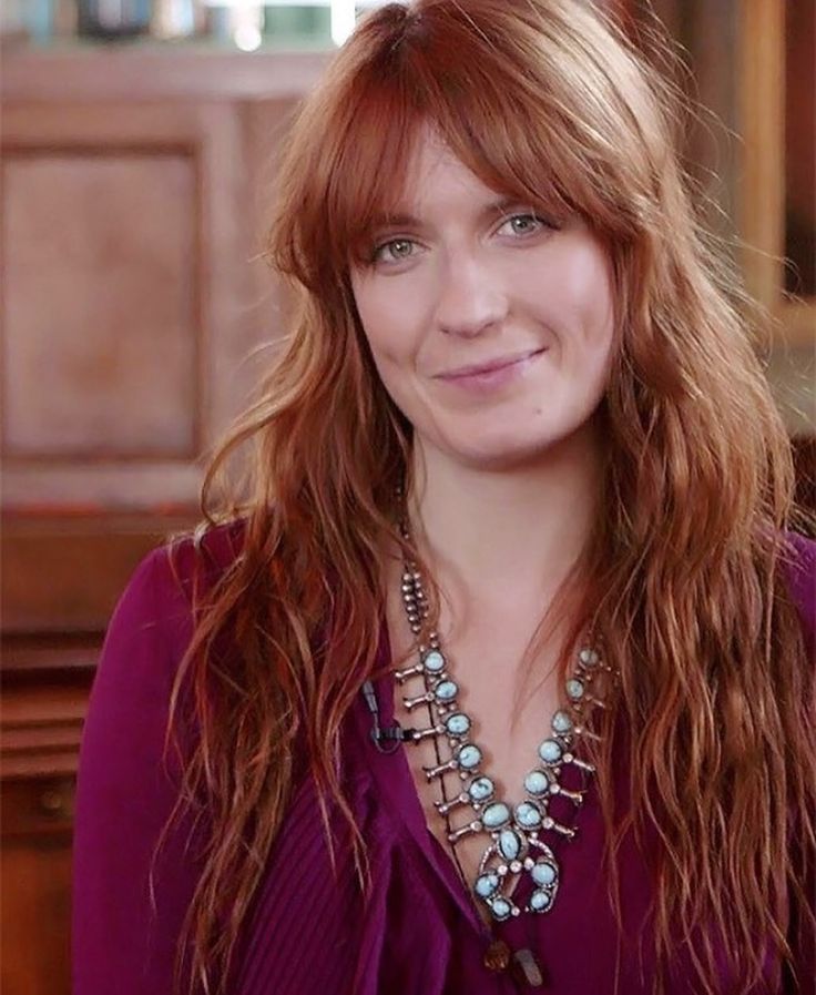 a woman with long red hair wearing a purple shirt and necklace smiling at the camera