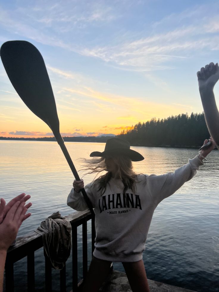 a woman in a cowboy hat holding two paddles over her head as the sun sets