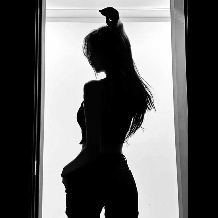 a black and white photo of a woman standing in front of a window with her back to the camera