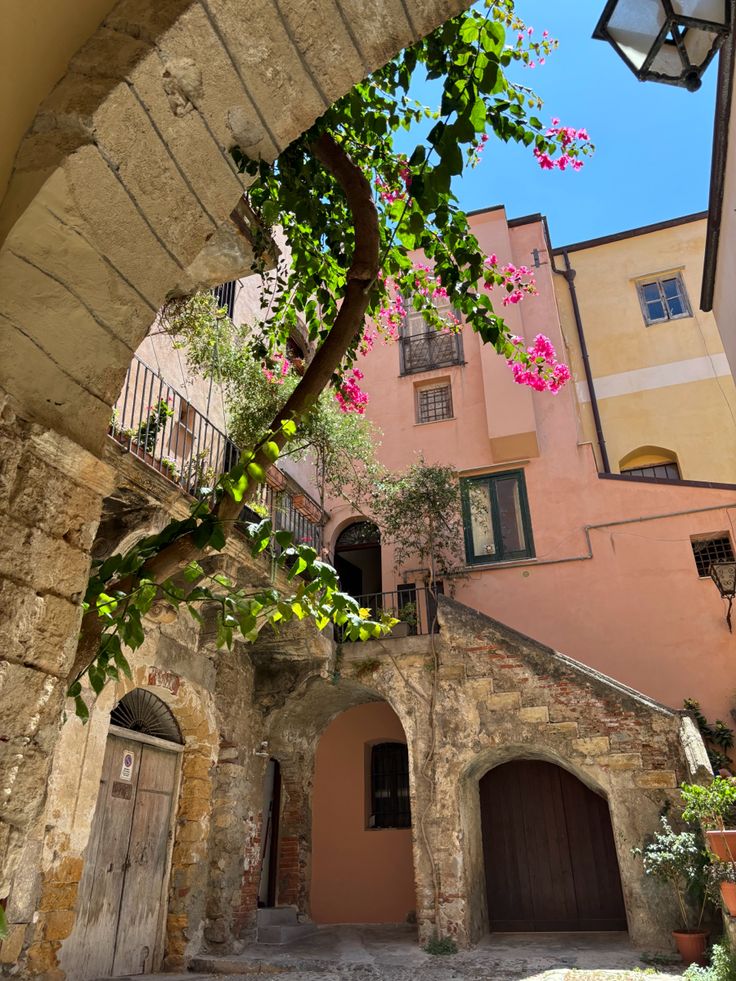 an archway leading to a building with pink flowers growing on the outside wall and door