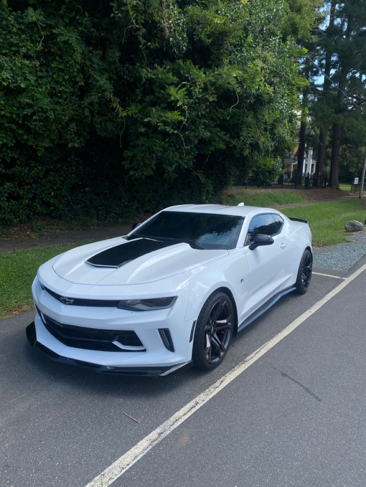 a white chevrolet camaro is parked on the side of the road in front of some trees