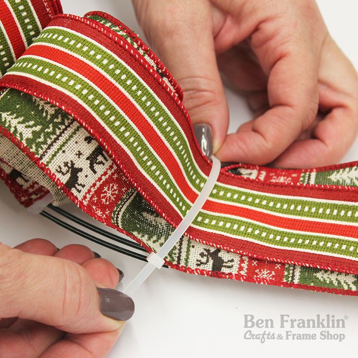 two hands are working on an ornament ribbon with red, green and white stripes