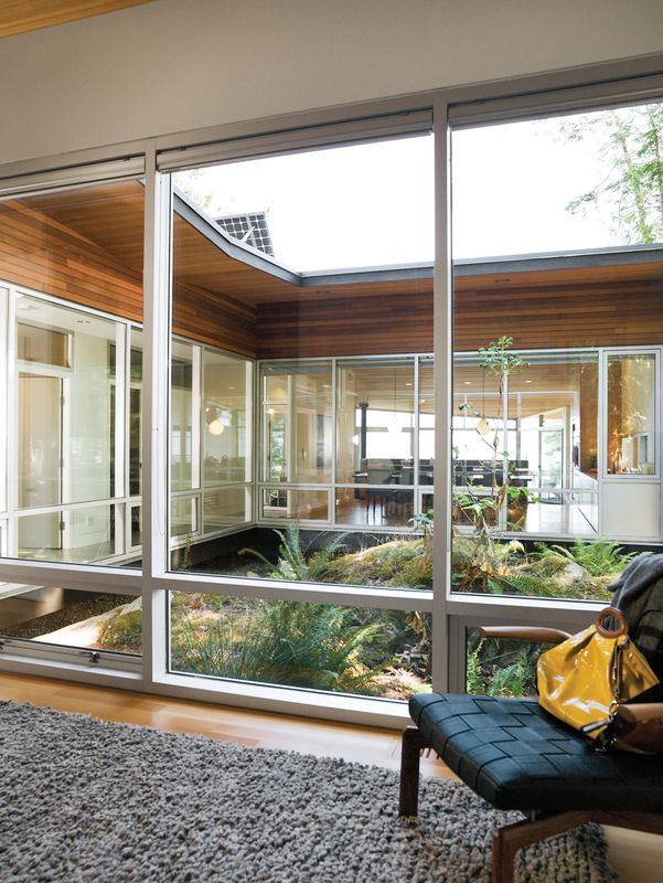 a person sitting on a bench in front of a glass wall looking out onto the yard