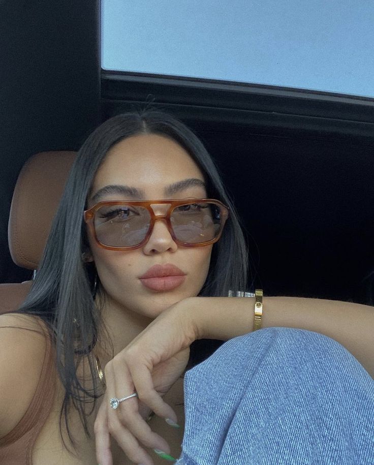 a woman wearing sunglasses sitting in the back seat of a car with her hand on her hip