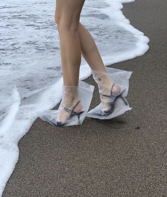 a woman's legs in clear plastic shoes on the beach