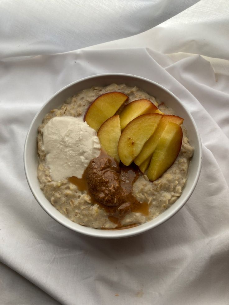 a bowl filled with oatmeal and sliced apples on top of a white cloth