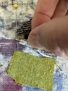 a person is stitching fabric with a sewing needle and yellow pin on the side