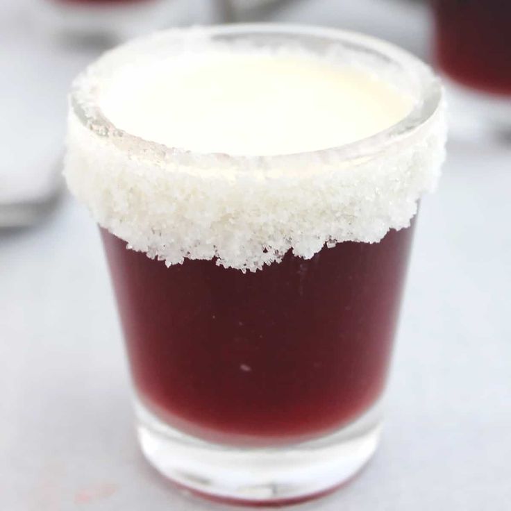 a shot glass filled with liquid and sugar on top of a white countertop next to other glasses