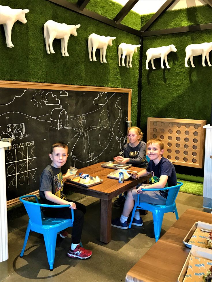 two boys sitting at a table in front of a chalkboard with farm animals on it